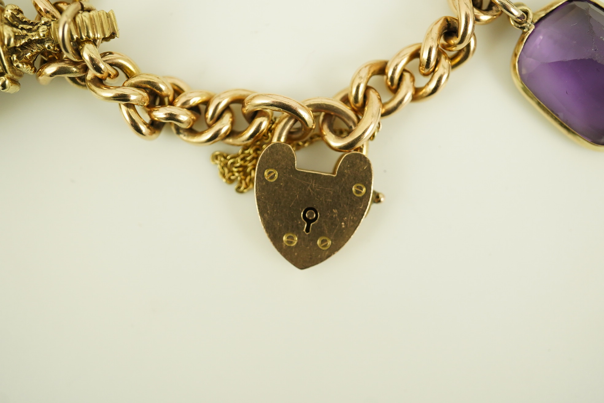 An Edwardian 15ct gold curb link charm bracelet with heart shaped padlock clasp, hung with six assorted gold overlaid and carnelian set fob seals